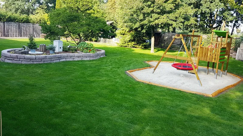Großer Garten mit Sitzbereich, Sandkasten und natürlichen Spielmöglichkeiten für Kinder