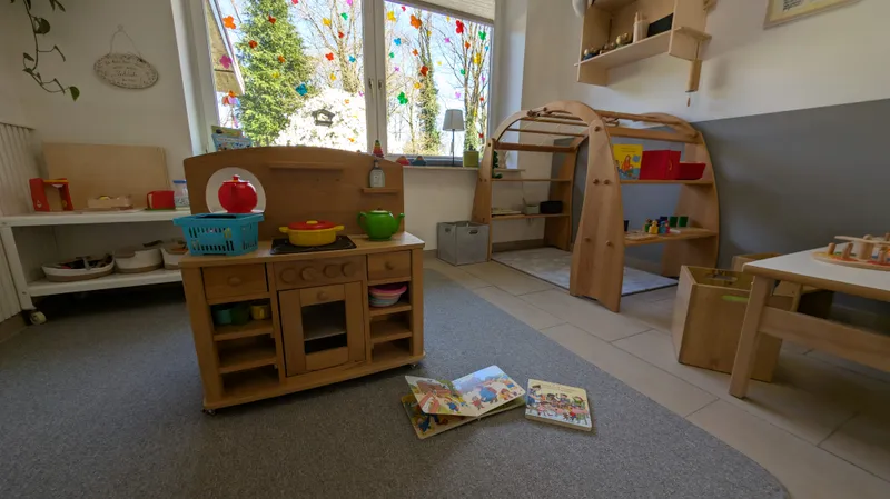 Kinderfreundlicher Spielbereich mit Holzküche und Bilderbüchern auf dem Teppich für spielerische Sprachförderung im Alltag