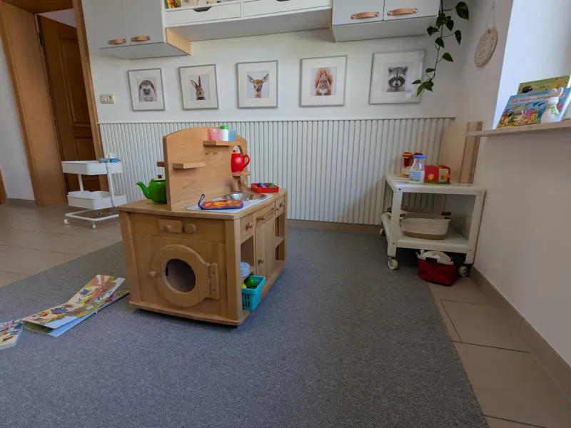 Gemütlicher Spielraum mit Kinderküche, Büchern und altersgerechten Spielmaterialien in warmer, einladender Atmosphäre